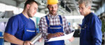 Drei Fachkräfte besprechen technische Unterlagen in einer modernen Produktionshalle.