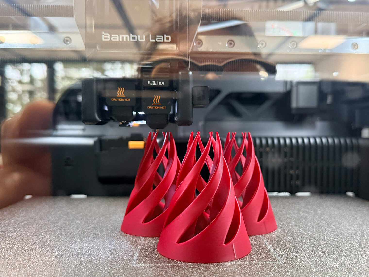 Drei rote 3D-gedruckte Objekte mit geschwungener Spiralform auf dem Druckbett eines Bambu-Lab-3D-Druckers im Kreativraum der BBT Tuttlingen.