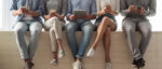 Fünf Personen sitzen mit Smartphones und einem Tablet auf einer Holzbank.